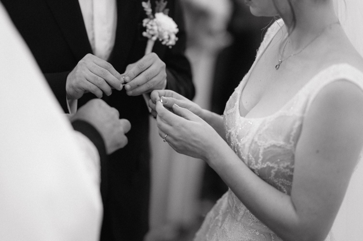 Closeup of bride and groom's hands during wedding ring exchange ceremony in black and white.