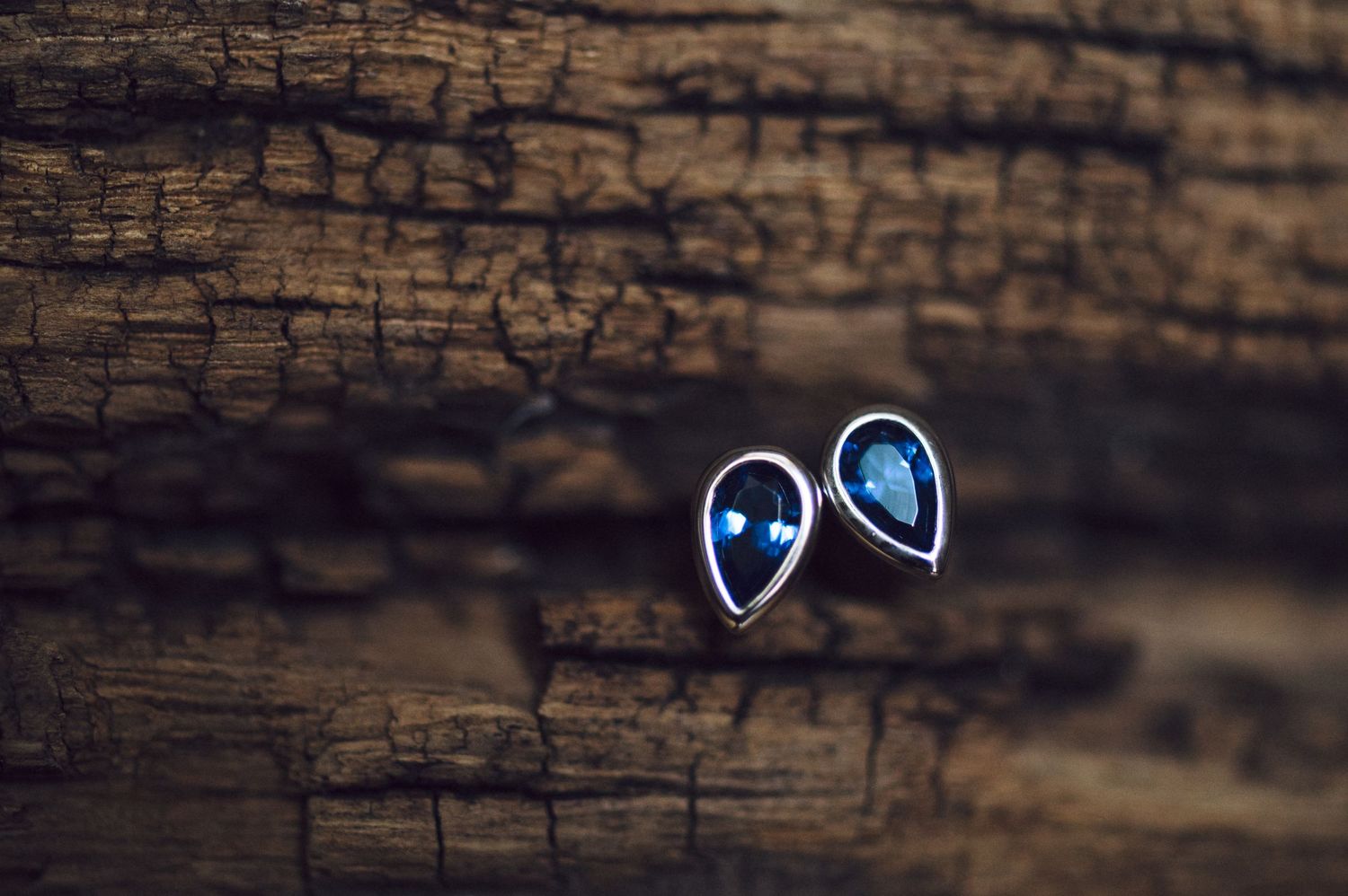 Two glowing blue teardrop-shaped rings rest on a dark wooden surface with textured grain patterns.