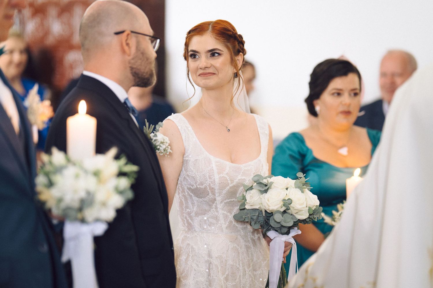 A wedding ceremony with the couple exchanging vows while guests watch and a person in teal stands nearby.