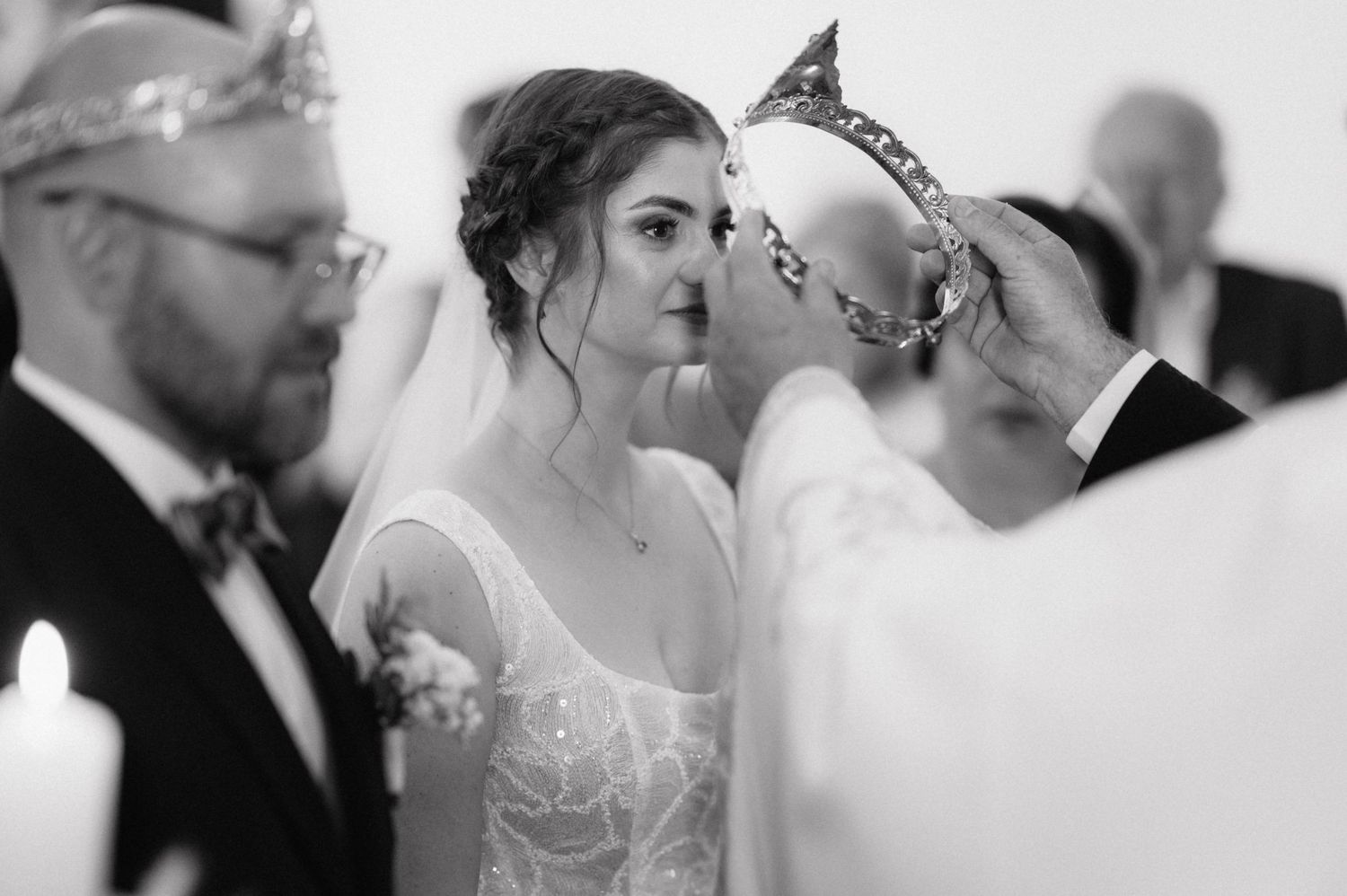 A wedding couple shares an intimate moment during their ceremony while guests look on in black and white photography.