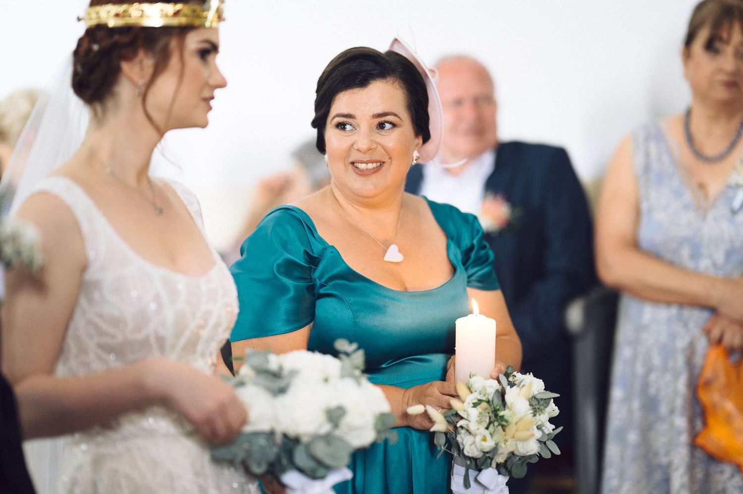 Wedding guests in teal and formal attire gather during a celebration, holding white bouquets.