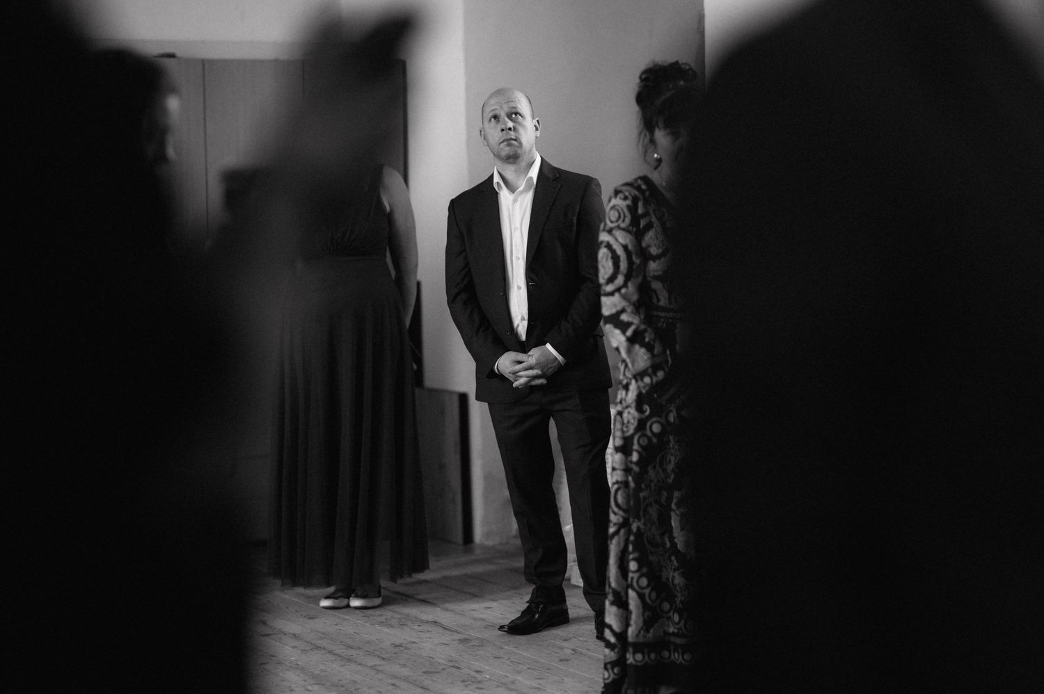 Black and white photo showing a person in a formal suit standing in a hallway between silhouettes of others.