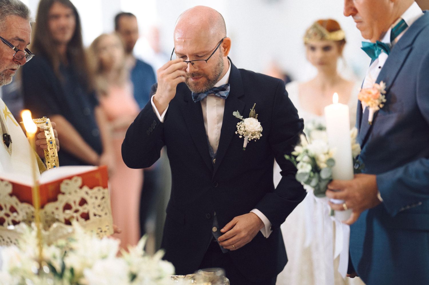 An emotional moment during a wedding ceremony shows a guest wiping tears while wearing a black tuxedo and bow tie.