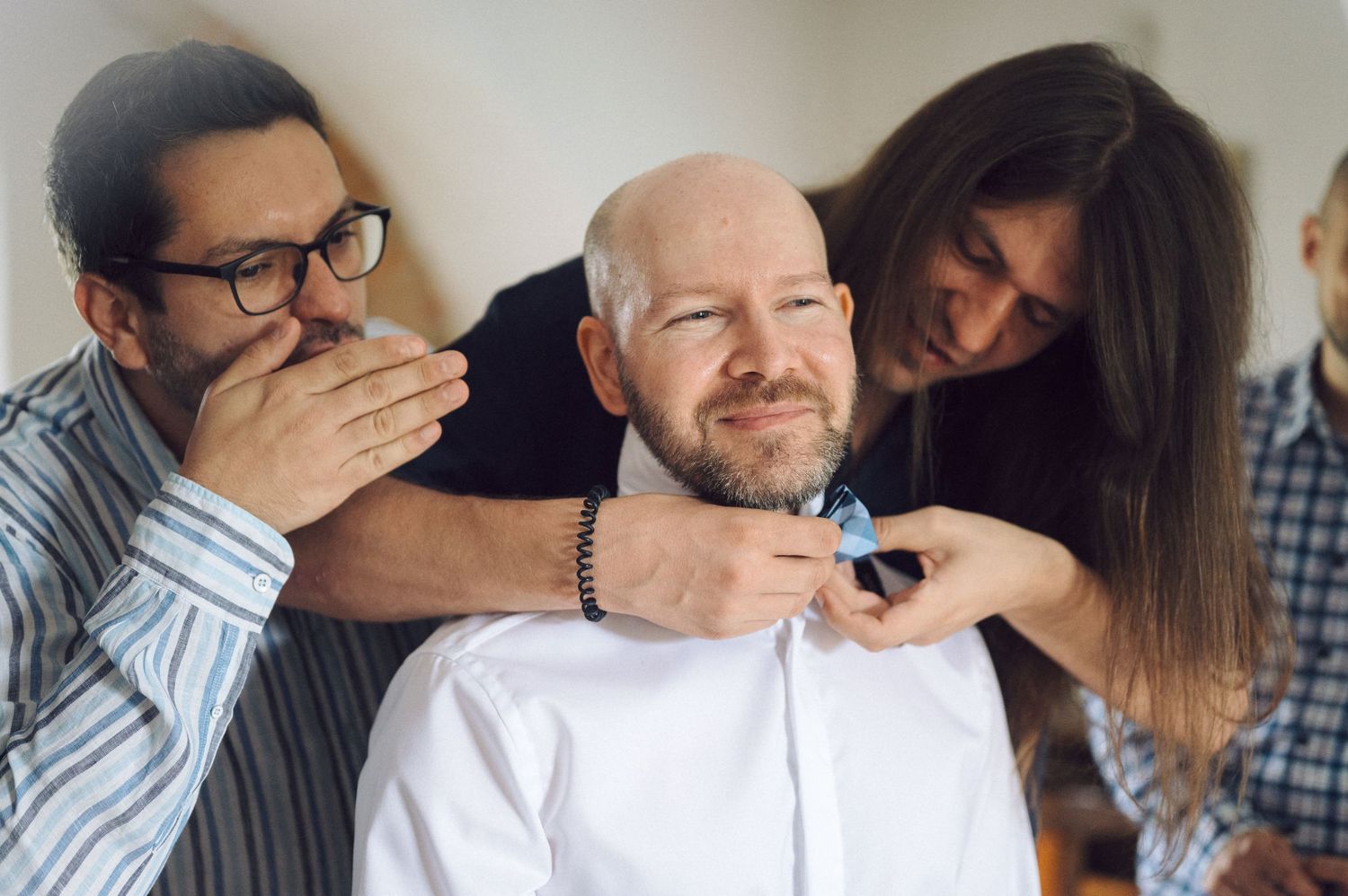 Three coworkers share a playful moment while grooming facial hair in an office setting.