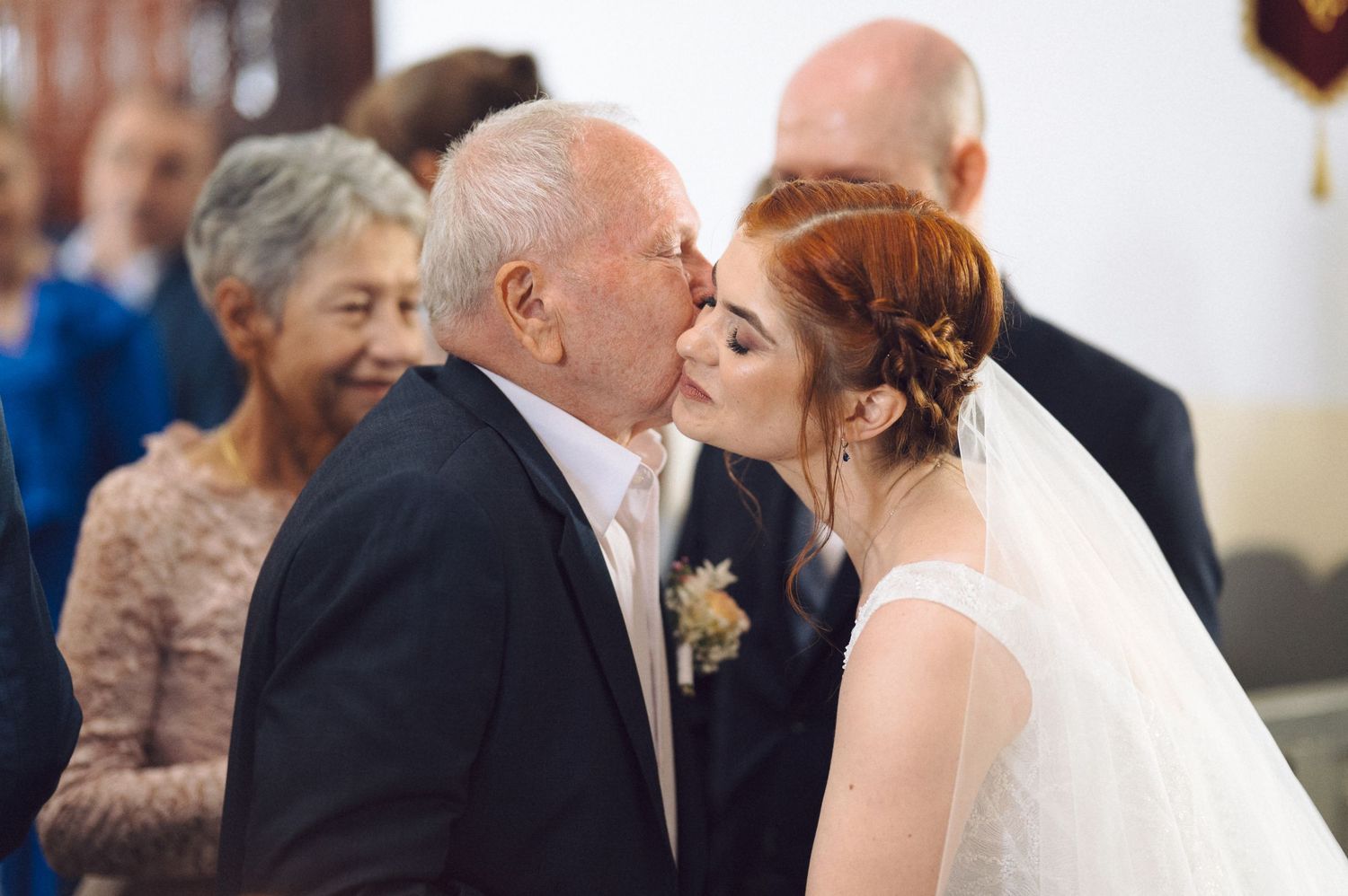 A tender moment is shared between the bride in a white veil and an older gentleman at a wedding celebration.
