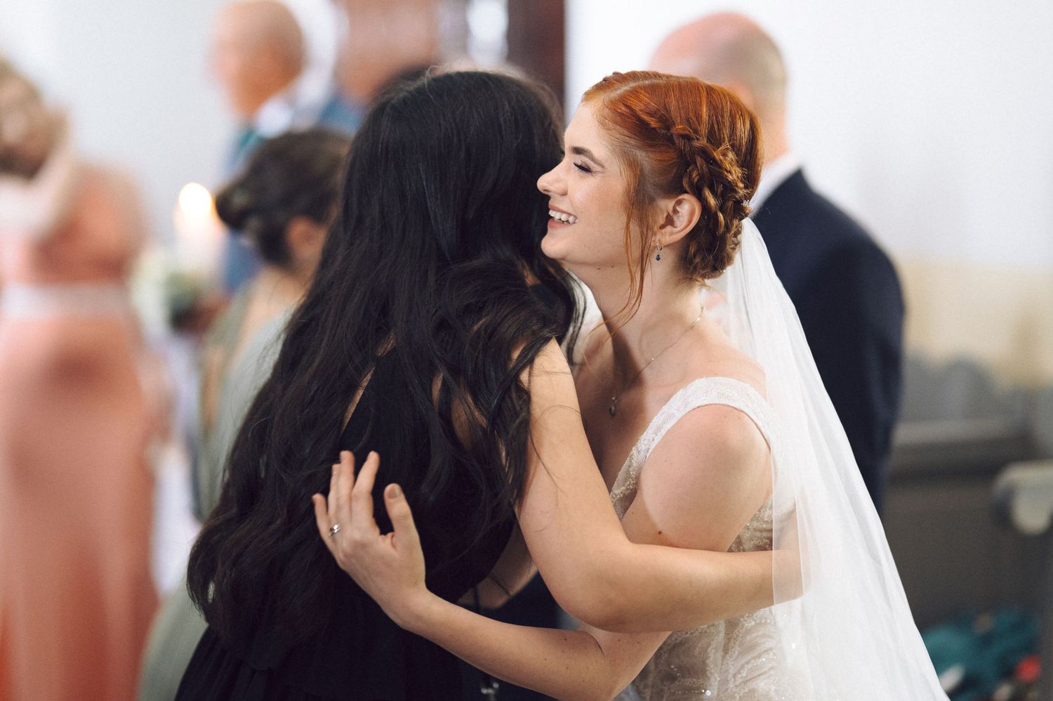 A bride in a white dress and veil embraces a guest during a wedding celebration.