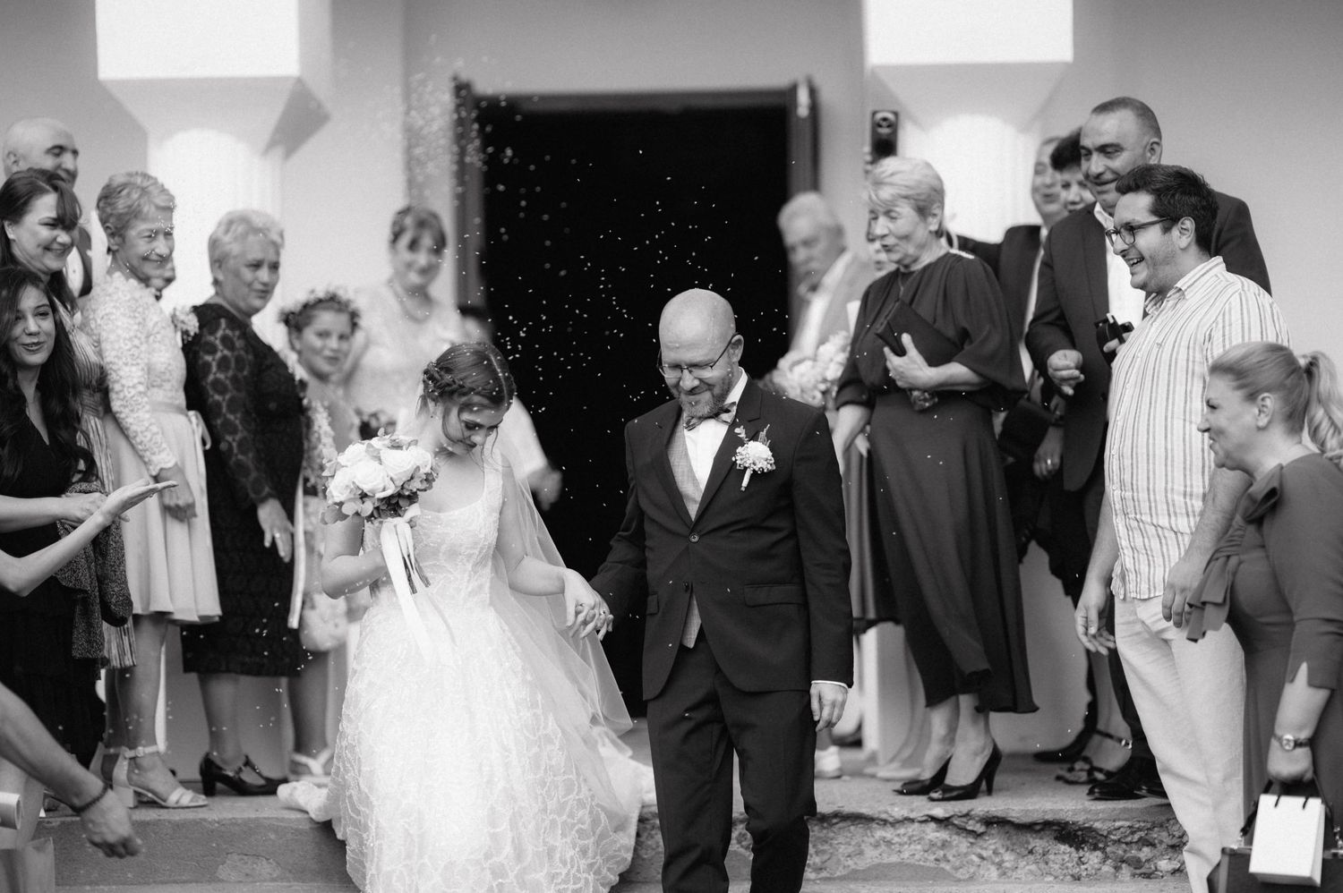 A joyous wedding celebration outside a church as attendees watch the newlyweds exit through white doors.