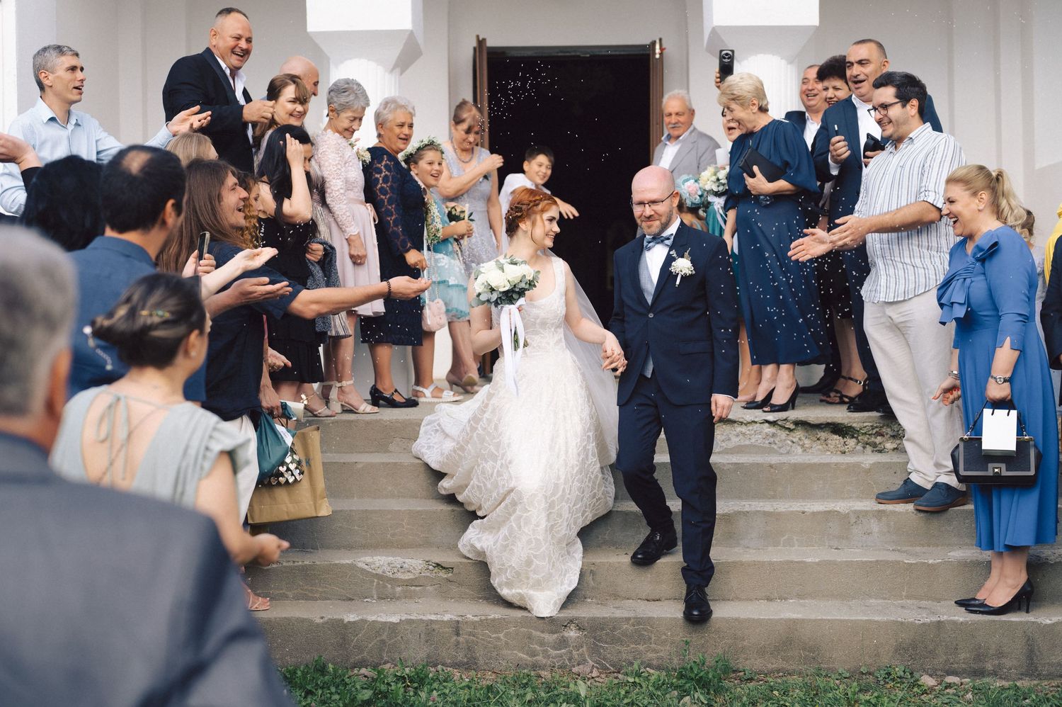 A joyous couple exits their wedding ceremony as guests cheer and throw flower petals on the church steps.