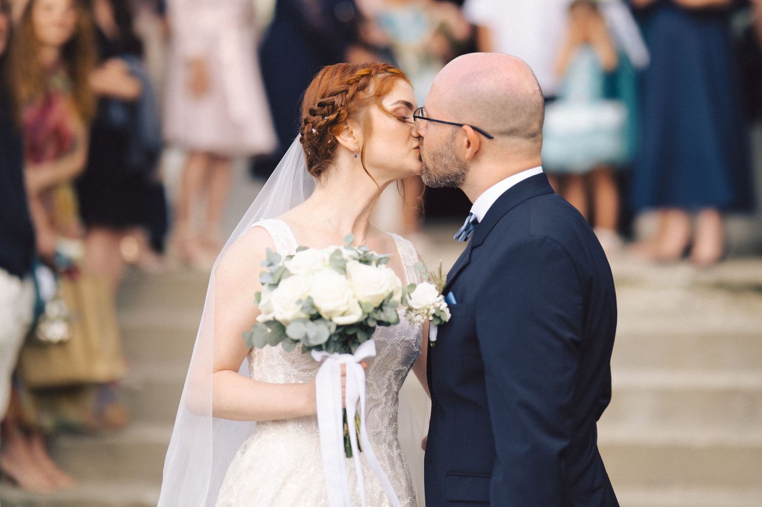A couple shares a romantic kiss during their wedding ceremony while guests look on in the background.