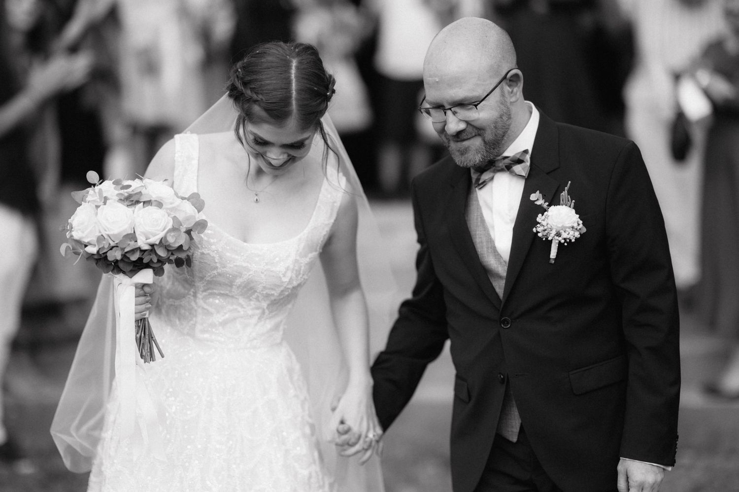 Black and white photo showing a groom escorting bride by the arm down a white-tiled outdoor walkway.