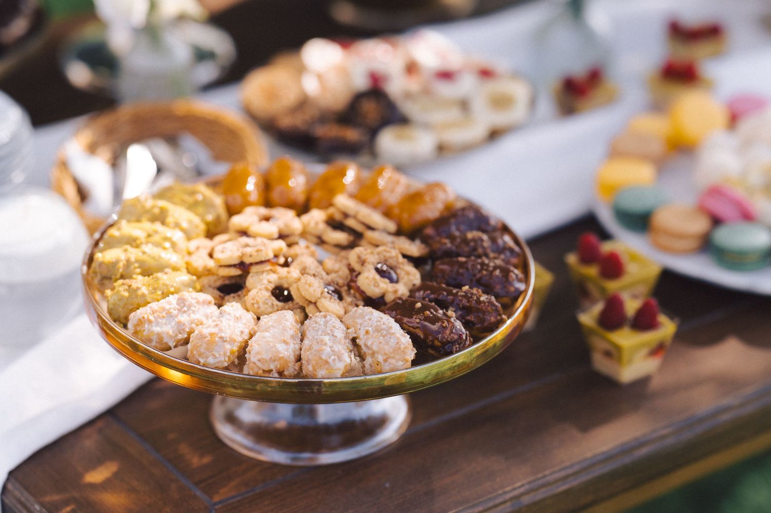 A table displays various delicious platters of cookies, pastries and bite-sized desserts at a catered event.