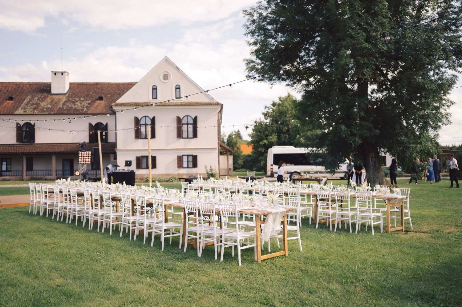 White wooden chairs arranged in rows on a lush green lawn for an outdoor wedding ceremony at a country estate.