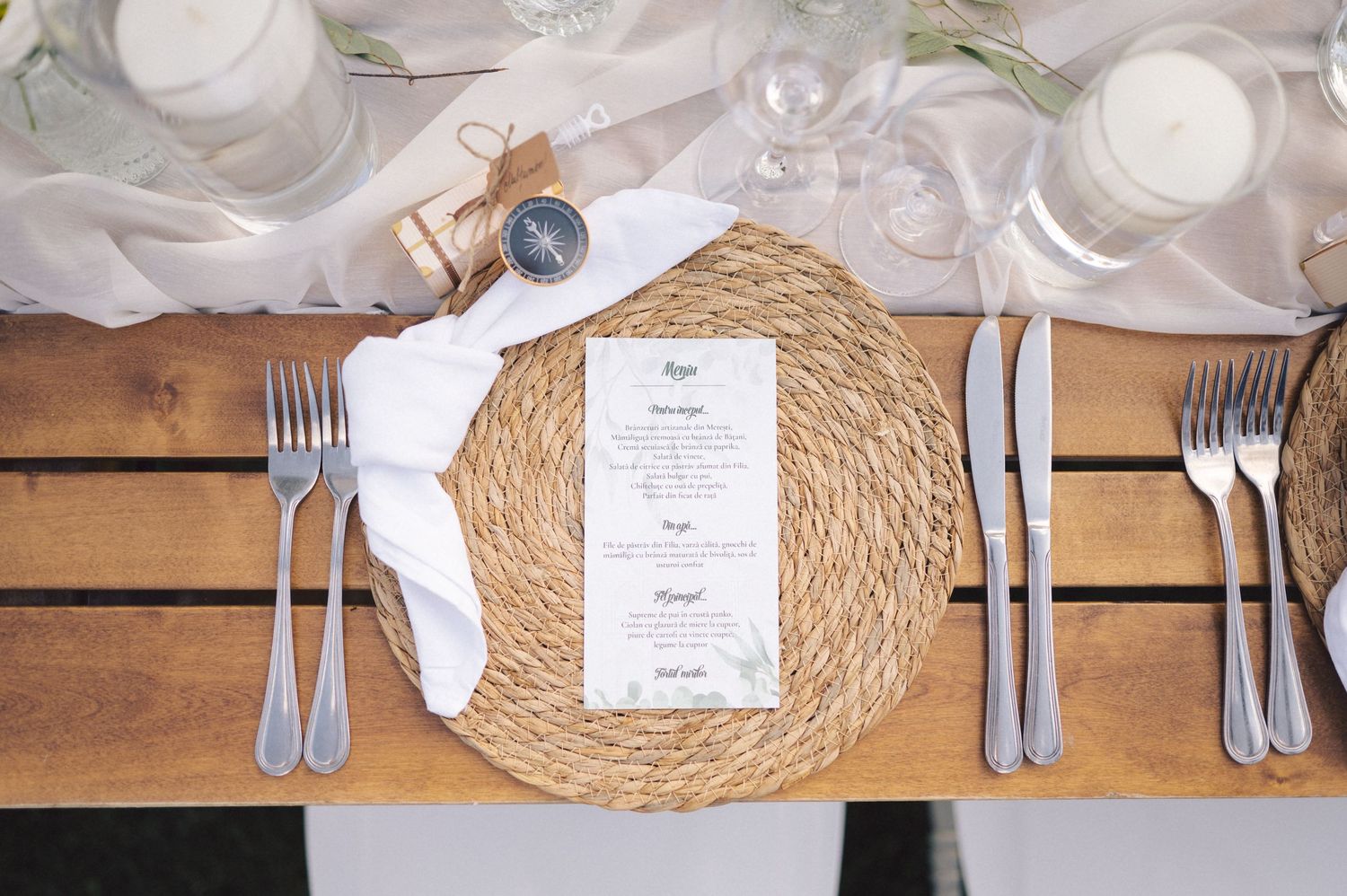 Place settings with woven placemats, silverware, and name cards arranged on a rustic wooden table surface.