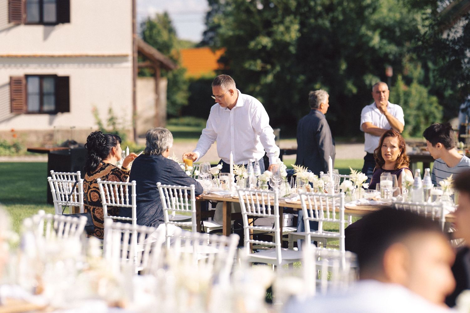 Outdoor wedding reception setup with white chairs and elegant table settings in a garden setting.