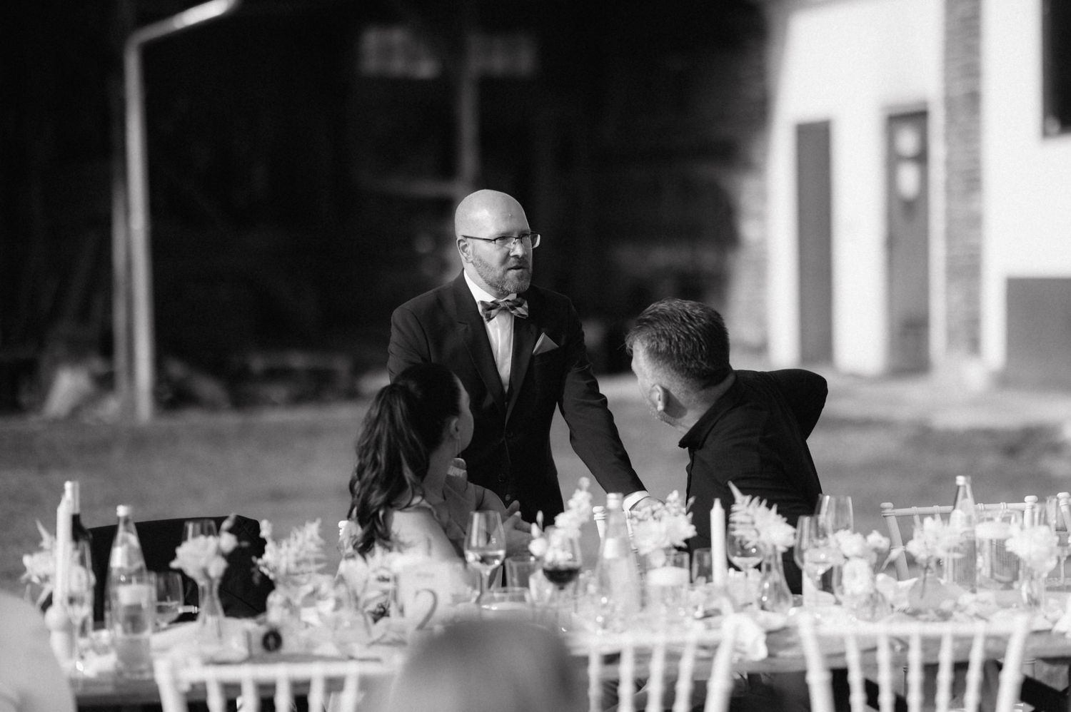 A monochromatic wedding reception table setup with elegant glassware and table settings glowing under soft lighting.
