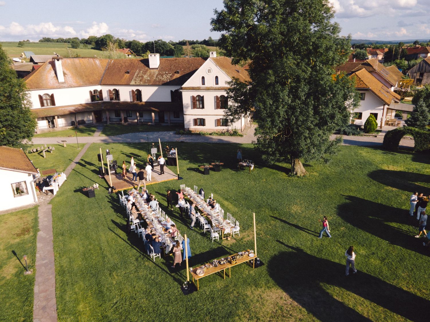 Aerial view of an outdoor wedding reception setup on a sunny day with white chairs arranged on a green lawn.