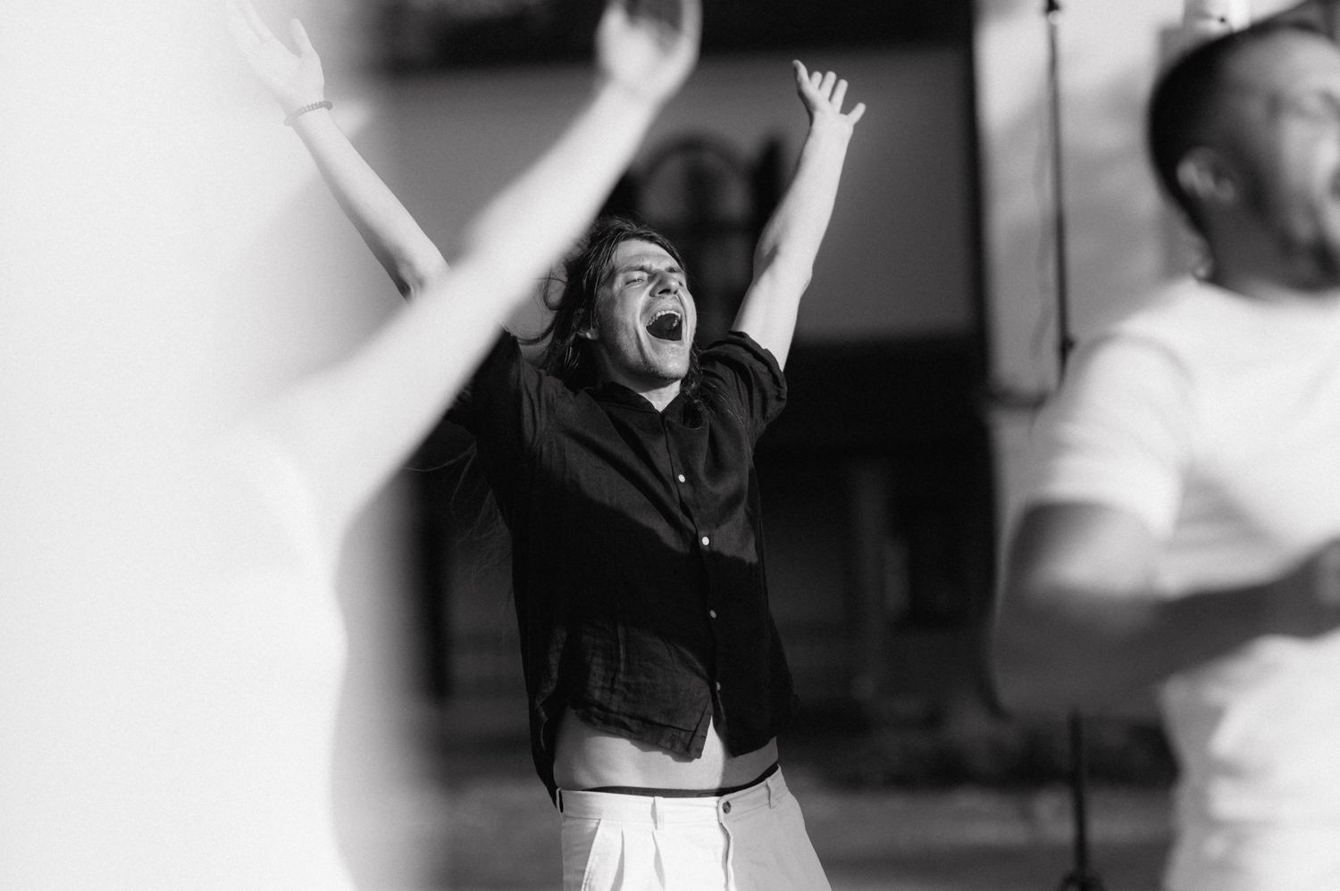 Black and white photo shows figure in dark shirt celebrating enthusiastically with arms raised overhead in victory pose.