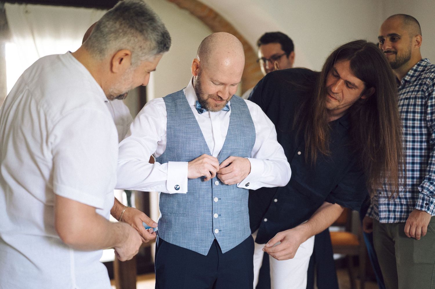 A small group gathers while adjusting formal attire and making final preparations before an event.