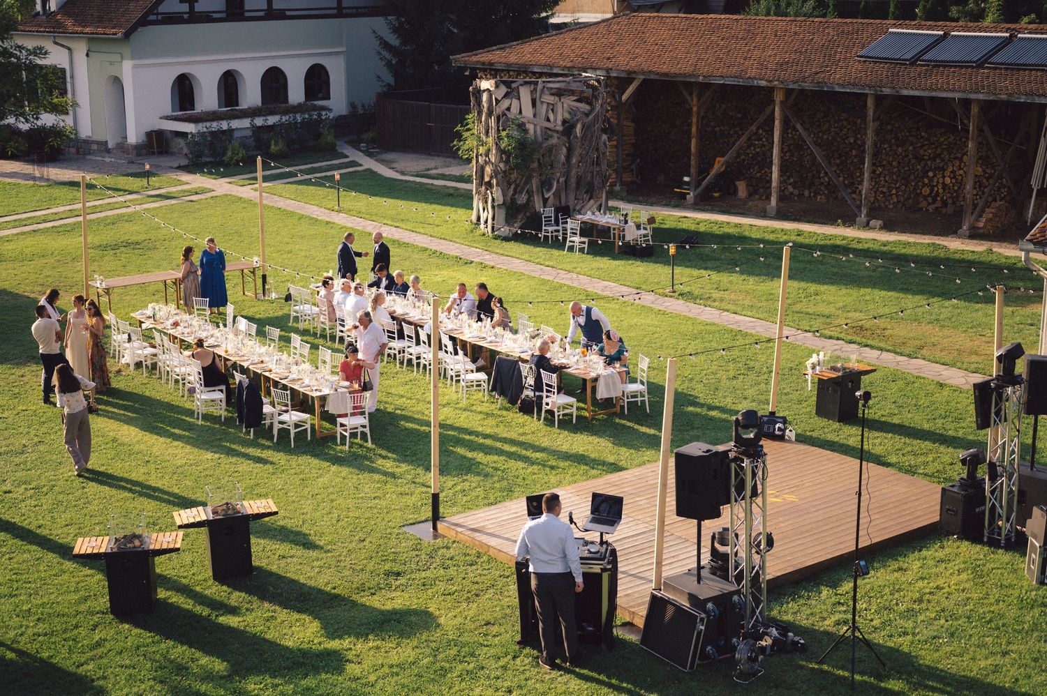 Long wooden tables and chairs set up on a green lawn for an elegant outdoor wedding reception celebration.