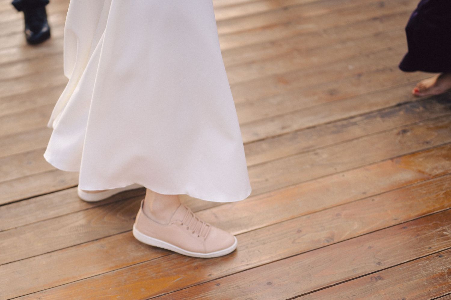 Wedding dress hemline and sparkly tennis shoes peek out against a wooden dance floor at a reception.