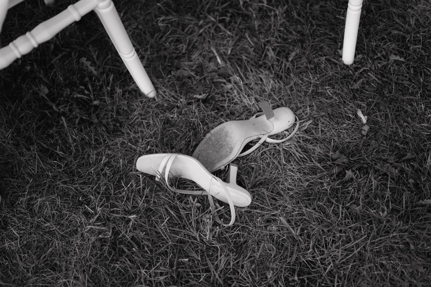 A pair of white ballet shoes lying discarded on grass in black and white photography.