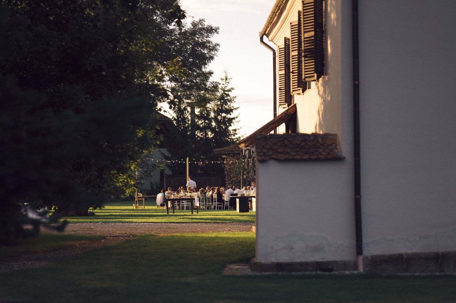 View of a historic white building corner at sunset with lawn and trees casting long shadows in the evening light.