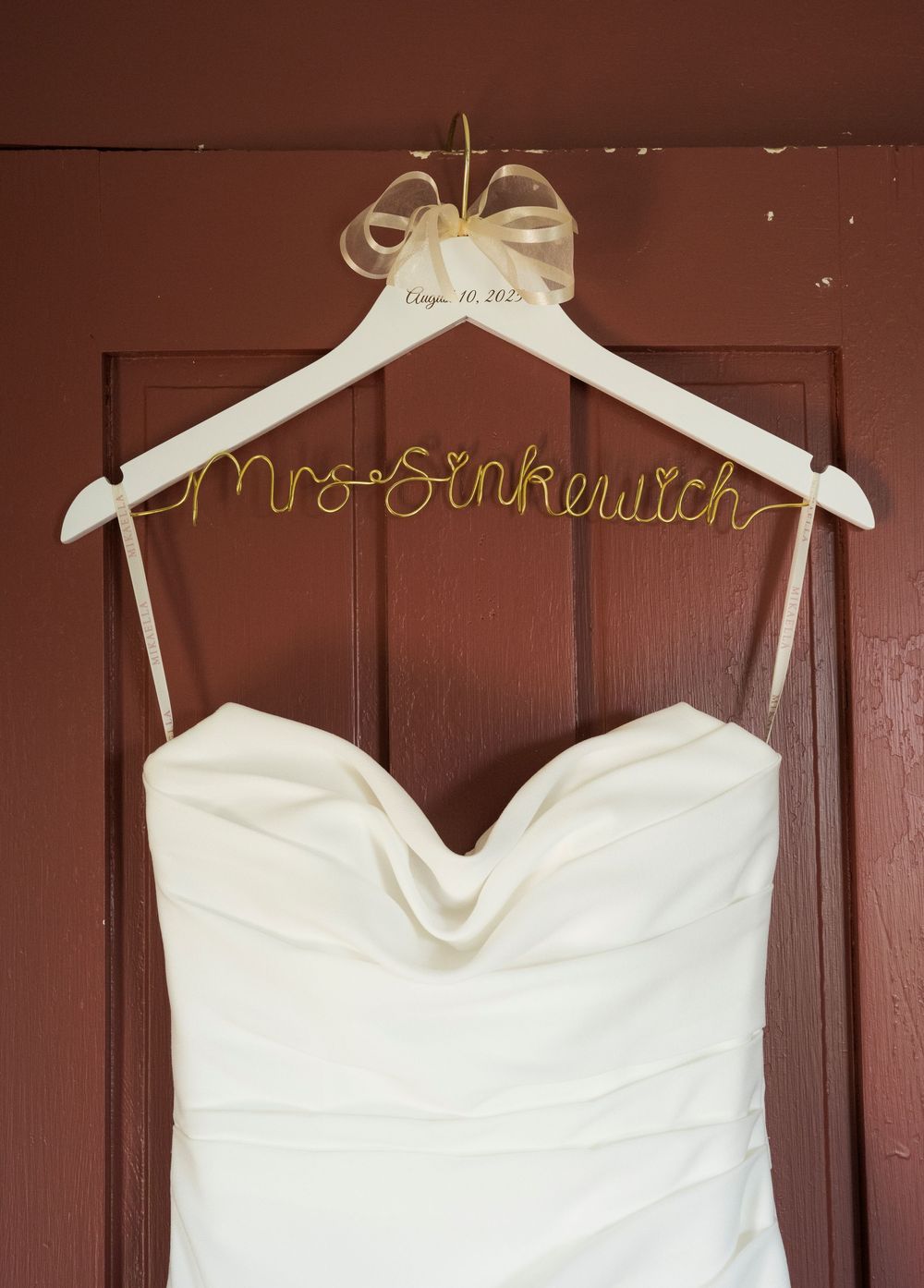 White wedding dress hanging on wooden hangers with custom name display.