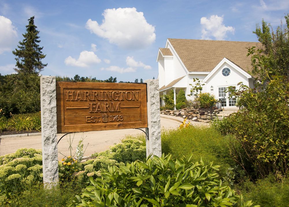 Charming white farmhouse wedding venue with wooden welcome sign and landscaped garden entrance.