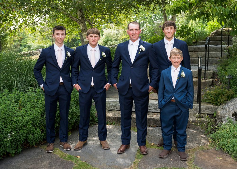 Groomsmen in navy suits pose for formal photo on garden steps.