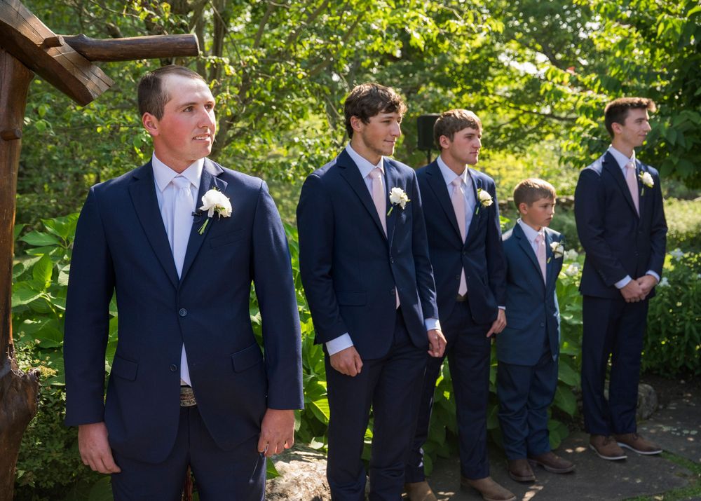 Wedding party in matching navy suits lined up outdoors for formal portrait.