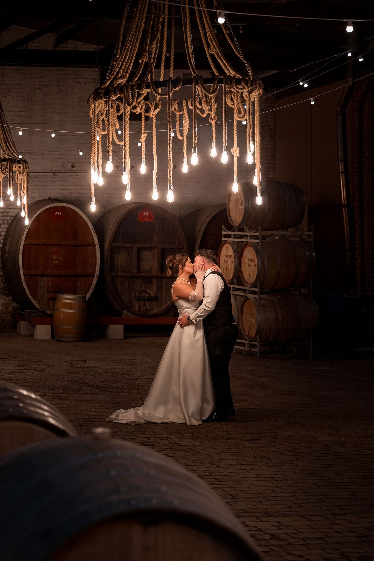 Bride and Groom sharing a moment kissing under a rope pendant light in the Grand Barrel Room during their wedding