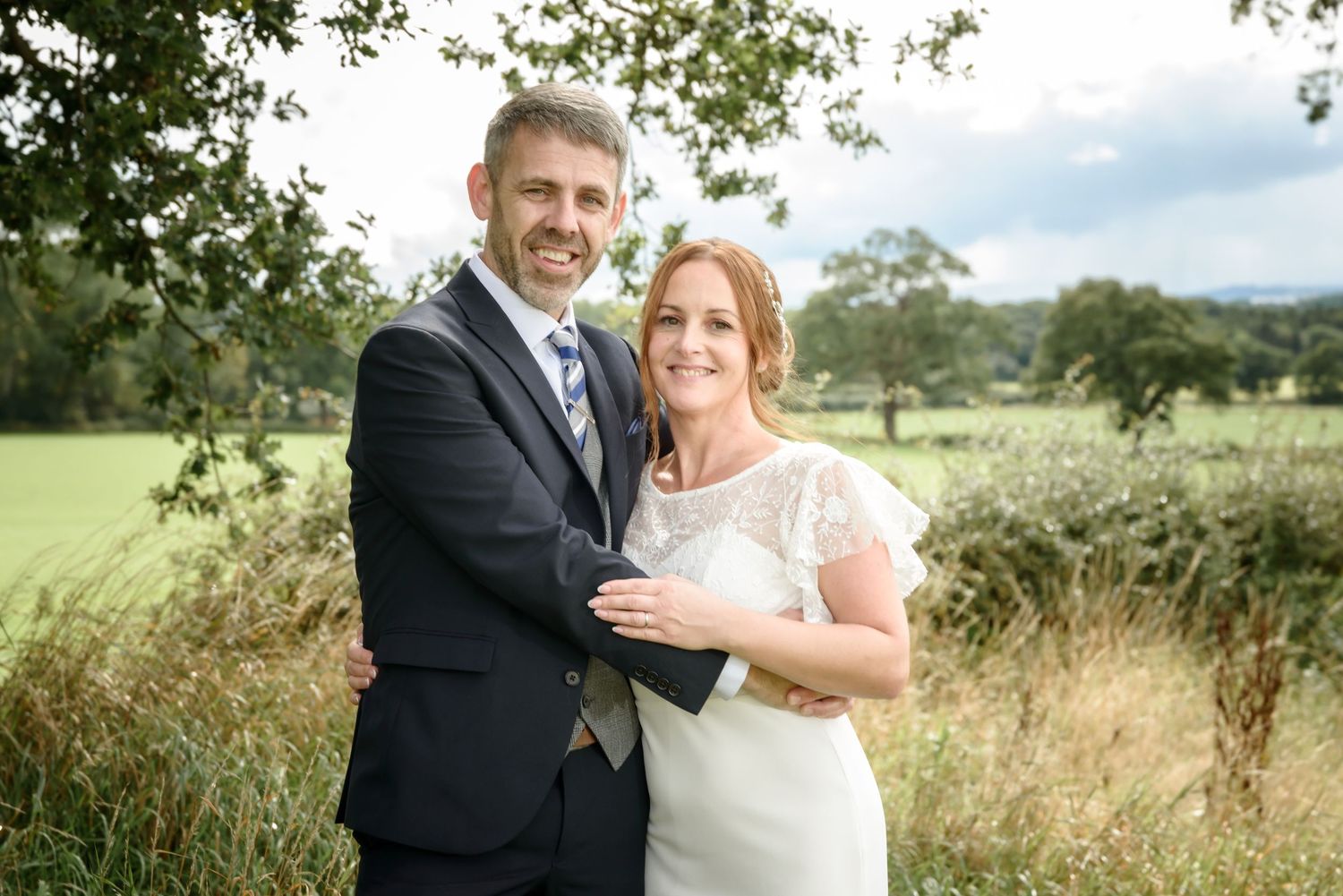 Newlyweds embrace in a romantic outdoor setting with lush greenery and natural lighting.