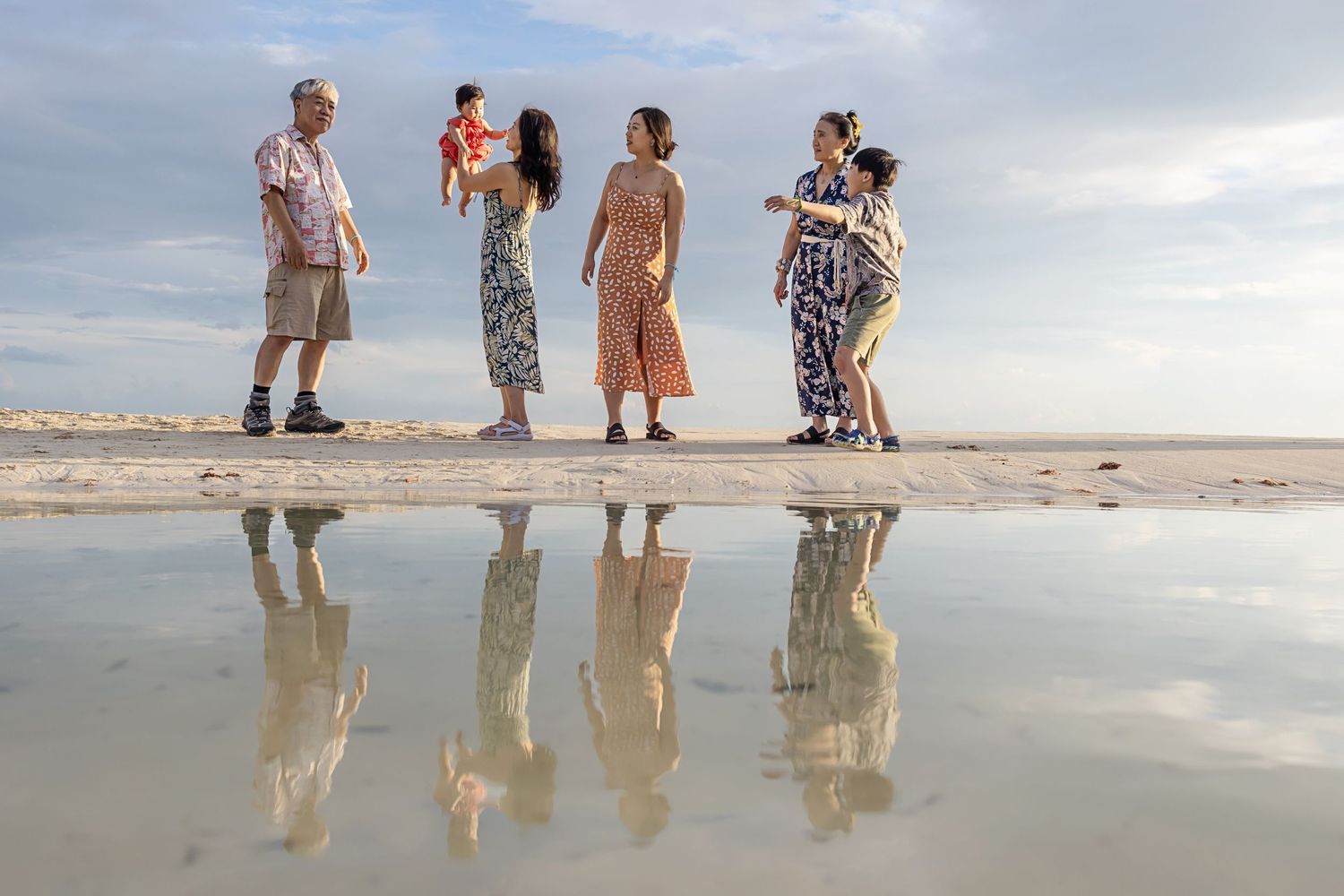 People walking along a reflective beach at sunset with their mirrored silhouettes visible in the wet sand.