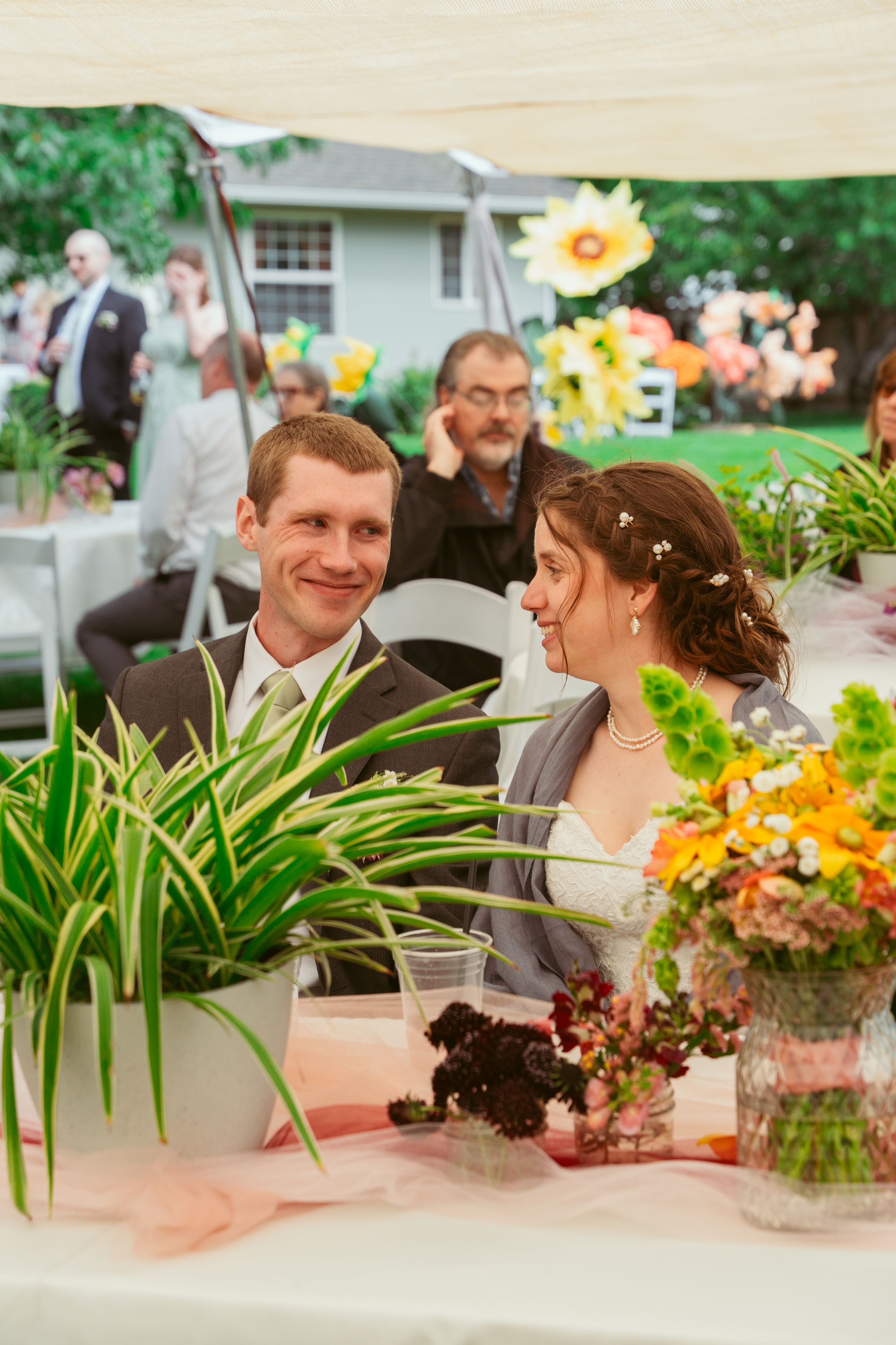 Wedding reception table decorated with yellow sunflowers and greenery as guests gather under a tent.