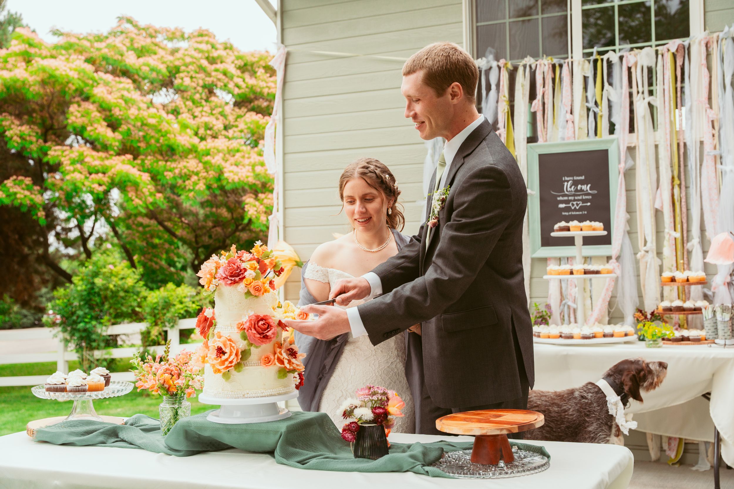 Couple cutting their wedding cake together at an outdoor reception with ribbon decorations.