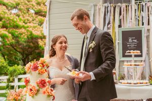 Newlyweds cut their wedding cake together at an outdoor reception with rustic decor and floral arrangements.