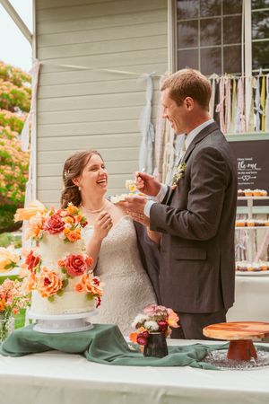 Newlyweds share a joyful moment while cutting their floral-decorated wedding cake at an outdoor reception.