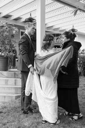 Black and white photo of wedding preparations on an outdoor porch with white pergola.