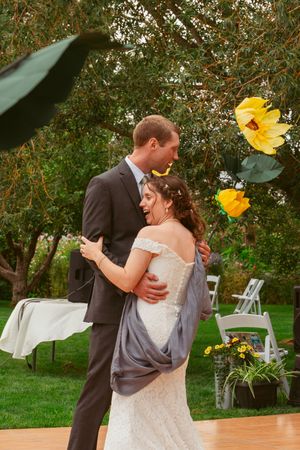 Couple sharing intimate dance moment on wooden dance floor with yellow flowers in background.