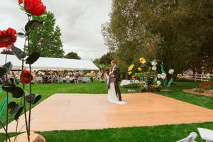 Wedding couple dancing on outdoor wooden platform with red and yellow flowers decorating the scene.