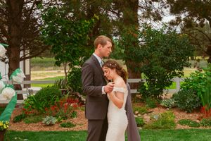 Couple dances intimately on wooden deck surrounded by lush garden greenery and trees.