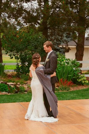 A couple shares a romantic dance moment on an outdoor wooden dance floor surrounded by flowers and landscaping.