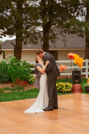 A romantic wedding couple shares their first dance on an outdoor wooden dance floor surrounded by colorful garden flowers.