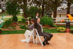 Wedding reception game with chairs on an outdoor wooden dance floor surrounded by garden landscaping.