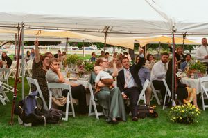 Wedding reception guests celebrating under a white tent with tables decorated with floral centerpieces.