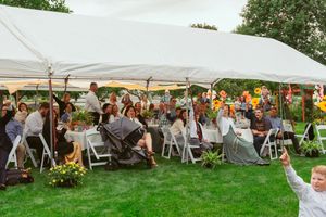 Outdoor wedding reception under a white tent with guests seated at tables decorated with colorful floral centerpieces.