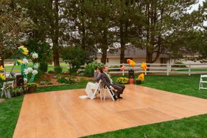An outdoor wedding dance floor set up in a backyard garden with colorful balloon decorations.