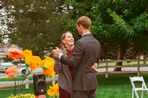 Couple dancing and smiling together near bright yellow flowers at outdoor celebration.