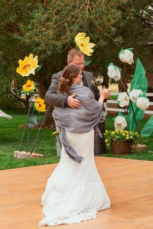 A newly married couple shares an intimate dance moment on an outdoor wooden dance floor near yellow sunflower decorations.