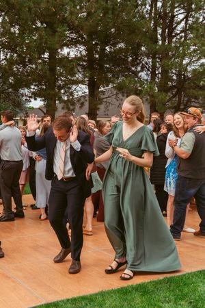 Wedding party and guests dancing in formal attire on an outdoor wooden dance floor.